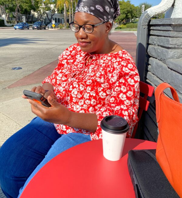 Tania sitting at a coffee shop table scrolling on cell phone